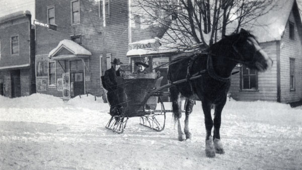 Courtenay’s Opera House is visible in the background of this image. It was near the corner of 5th Street and Cliffe Avenue. R. Merle Halliday (1875-1944) and his wife Jessie (1887/1888? – 1936) are in the horse drawn cutter. The horse (Tammy) and cutter were owned by Reverend Menzies. Date: winter of 1915-1916. CDM 980.39.2 